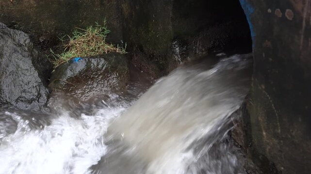 A strong stream of water gushes out of a concrete pipe or large culvert into a lower irrigation channel, creating a powerful foam, and indicating a controlled release of water.