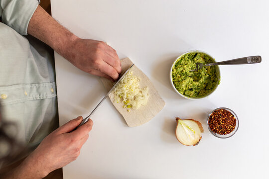 POV man hands cutting onion on wooden cutting board with green pesto chili whole onion. Guacamole preparation home cooking fresh ingredients