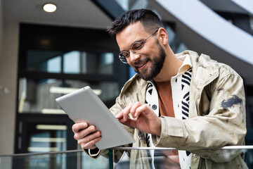 Young professional in a modern business district smiles at a tablet during a video meeting reviewing project updates, checking schedules and coordinating tasks on the go between buildings in the city