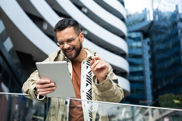 Young professional in a modern business district smiles at a tablet during a video meeting reviewing project updates, checking schedules and coordinating tasks on the go between buildings in the city