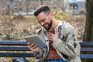 Fototapeta premium Cool freelance professional work from park bench with tablet, replying to clients, reviewing briefs, scheduling calls, staying productive outdoors flexible, mobile, connected while enjoying fresh air