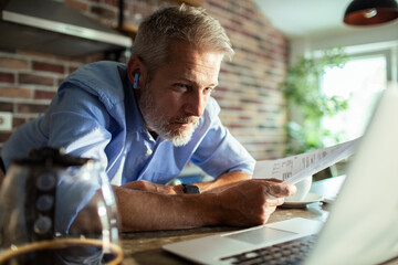 Mature man focused reviewing bills at home kitchen