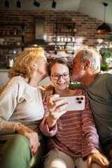 Happy grandparents kissing teen granddaughter taking selfie at home