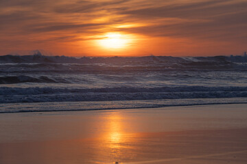 Fototapeta premium Atlantic sunset with rough waves and golden reflection on sandy beach