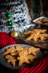 A cozy holiday scene featuring homemade gingerbread man cookies arranged on a striped plate, with additional cookies displayed in a glass dish in the background. 