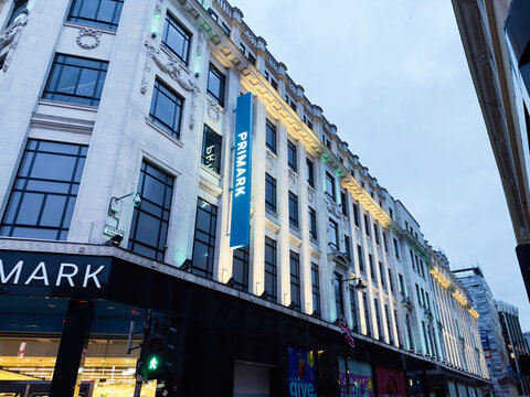 City street in Manchester with Primark storefronts and illuminated historic buildings at dusk