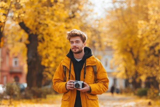 A stylish young man strolls through a picturesque autumn park surrounded by golden leaves taking photos with a vintage film camera Creative fall pastime