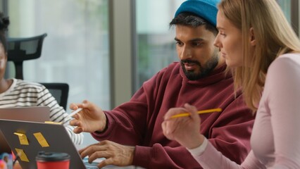 Pensive thinking Arabian informal business man Indian male worker startup founder working with laptop typing writing notes in office casual businessman job concentrated with two multiracial women