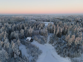 Drone view of snow-covered trees and open forest glades beneath a glowing orange sunset sky