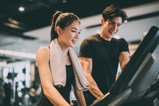 A slender Asian woman exercises on a treadmill with her trainer in the gym promoting her healthy lifestyle through cardio for weight loss