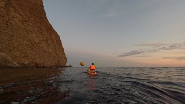 Kayaker ocean sunset paddling along tranquil cliff at dawn scenic adventure - Powered by Adobe