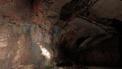 Inside a magnificent cave, light shines on the rugged walls, revealing stunning rock formations. The atmosphere feels ancient and mysterious, inviting adventure and exploration.