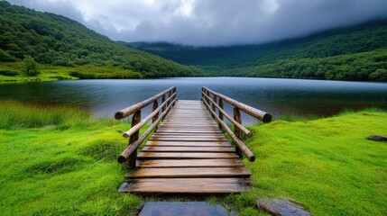 A wooden boardwalk guides visitors to a calm lake, nestled among verdant trees and grassy areas. The cloudy sky suggests a peaceful yet moody atmosphere, ideal for nature exploration