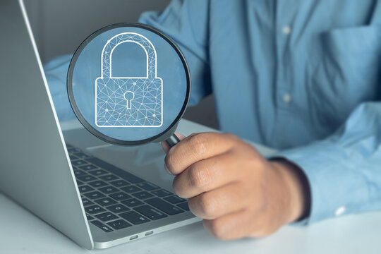 Cybersecurity concept. Businessman using magnifying glass to check padlock icon on laptop. Data protection, internet privacy, and network security analysis.,copyspace for put text or logo.