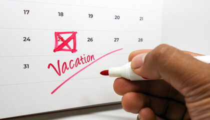 A hand marking Vacation and crossing out the 25th on a calendar with a red marker.