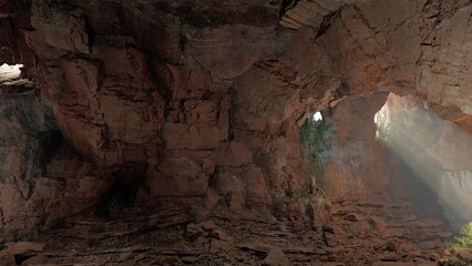 Natural wonders of a hidden cave reveal stunning rock formations and lush greenery. Sunlight casts ethereal rays, highlighting the beauty of this secluded location in nature.