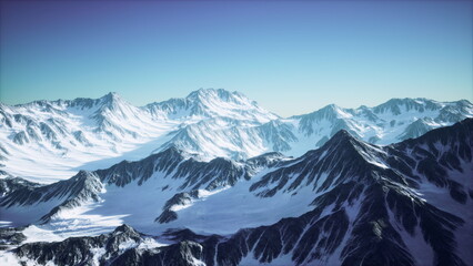 Fototapeta premium Snow blanketed peaks rise majestically against a bright blue sky at dawn. The landscape showcases rugged terrain, with sunlight illuminating the mountain ridges and valleys below.
