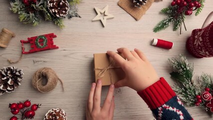 Top-view 4K footage of hands wrapping a holiday gift with rustic twine and festive decorations on a wooden table