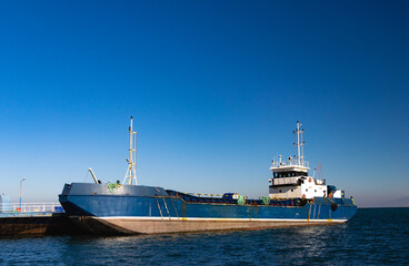 Obraz premium An empty blue container ship anchored in a small harbor. An empty cargo ship on a gently choppy sea under a blue sky. Transportation and sea transport.