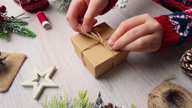 Slow motion footage of hands tying rustic twine on a small holiday gift box surrounded by festive decorations