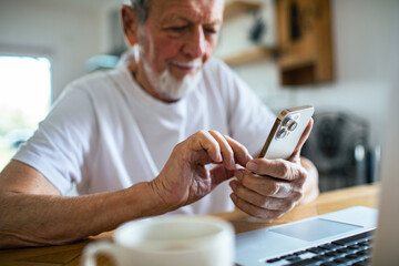 Senior man content using smartphone at kitchen table