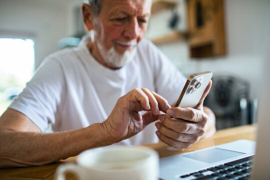 Senior man content using smartphone at kitchen table