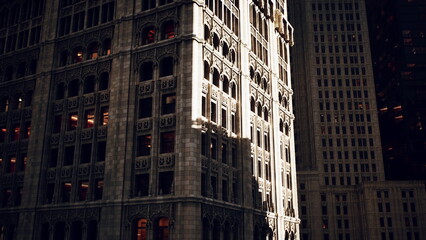 Fototapeta premium Intricate stonework of a historic building stands out against contemporary structures. The late afternoon sun casts long shadows, creating a striking contrast between eras in the city.