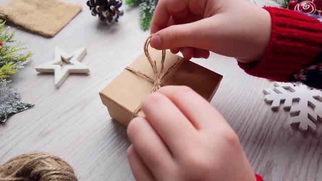 Slow motion close-up of hands tying a bow on a small kraft gift box during festive holiday wrapping