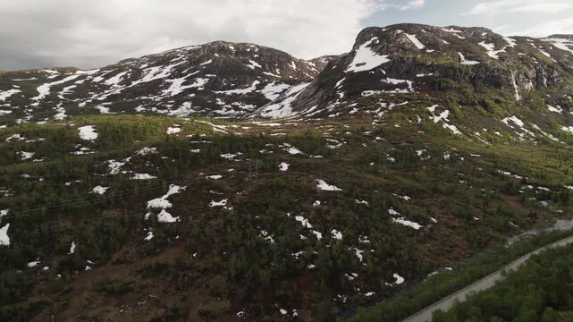 Aerial view of rugged mountains interspersed with snow and greenery under a cloudy sky, creating a dramatic contrast of textures, Dalen, Telemark, Norway.