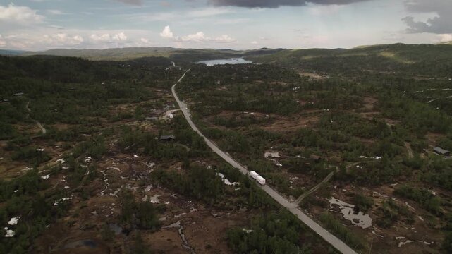 Aerial view of a winding road cuts through a dense forest leading towards a serene lake in the distance, Dalen, Telemark, Norway.