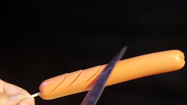 Grilled Sausage Being Sliced with Knife on Black Background