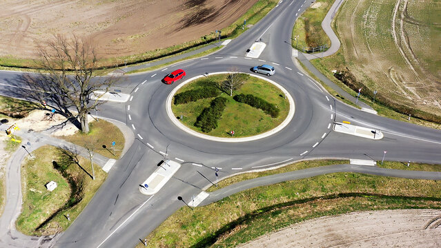 Aerial view of a rural roundabout with cars navigating circular intersection, surrounded by fields and sparse trees