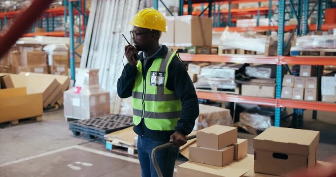 Logistics, radio or black man in warehouse with package, communication or inventory management in supply chain. Feedback, trolley or loader in depot with tech, ppe or cargo update for distribution.