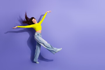 Young beauty woman in neon yellow top jumping with joy against purple background showcasing fashion lifestyle and happiness