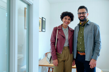 Young adult Caucasian man and young adult Black woman standing together smiling in modern room, both looking at camera, showing friendly expression and casual posture