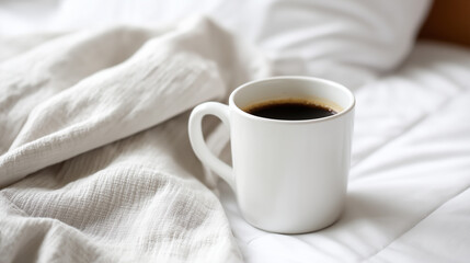 Warm cup of black coffee resting on soft white bedding.