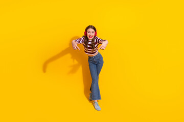 Young girl dancing in a striped top jeans and headphones against a bright yellow background