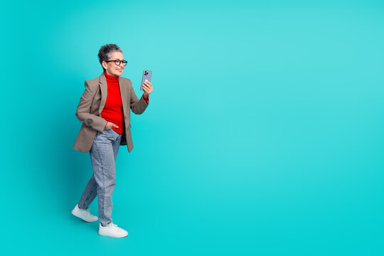 Stylish mature businesswoman in red turtleneck blazer walking checking her smartphone teal backdrop for modern professional lifestyle image