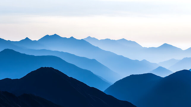Layered mountain ranges fade into the distance in hues of blue, creating a serene and calming landscape. The silhouette of the peaks blends with the misty horizon.