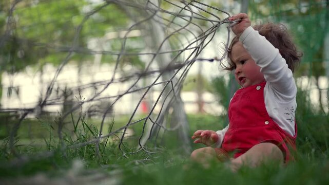 Toddler sitting on grass exploring soccer net, pulling strings with hands, showing curiosity and concentration in playful moment of early learning and discovery