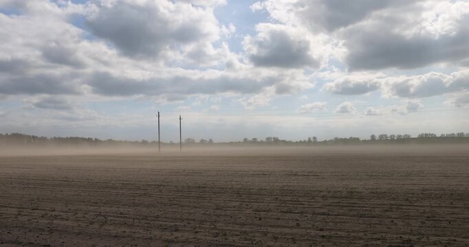 dust storm in windy weather in the field after plowing and preparing the field for sowing, flying dust from strong winds in the agricultural field in the spring season, blue sky with clouds