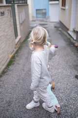 Little 4 Year Old Girl Walking Through Narrow Streets with a Scooter Without a Helmet