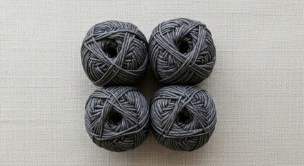 Four gray yarn balls on beige textile for knitting and crochet projects