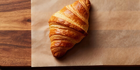Golden flaky croissant resting on parchment paper with warm lighting, perfect for breakfast or bakery promotions, evoking delicious comfort and artisanal quality.