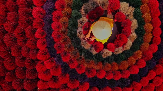 Aerial view of colorful concentric circles of incense sticks with a woman wearing a traditional hat, inciense town, Hanoi, Vietnam.