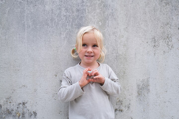 Little 4 Year Old Blonde Girl Standing by a Wall, Pretending to Be Angry and Showing Claws