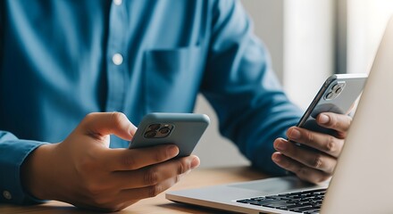 Person holding two smartphones while sitting at a desk with a laptop technology mobile