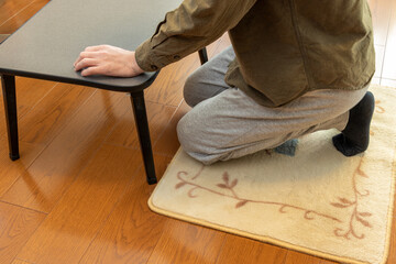 床に敷いたカーペットの上に座ろうとする男性