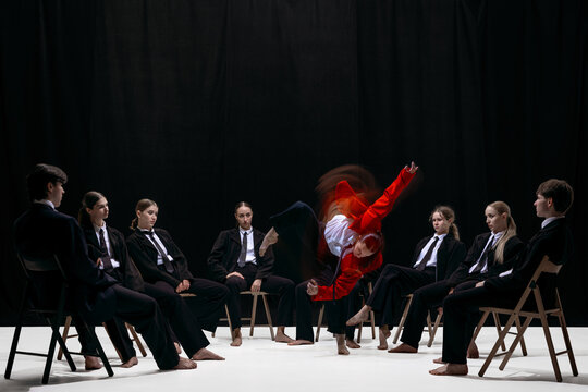 Blurred dynamic jump of person in red jacket surrounded by seated group symbolizing breakthrough and innovation. Concept of startup energy, disruptive thinking, future mindset and creative movement.