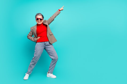 Senior woman in red turtleneck jacket and jeans poses joyfully on turquoise background for lifestyle fashion advertisement and promotion - Powered by Adobe